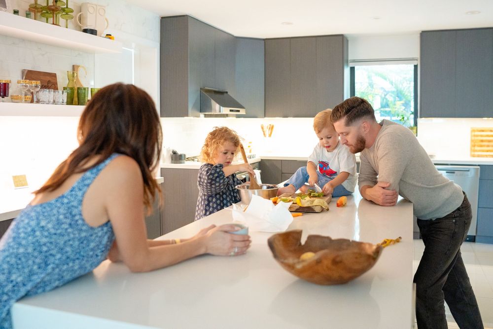 Family gathered around white kitchen counter enjoying snacks and conversation together.
