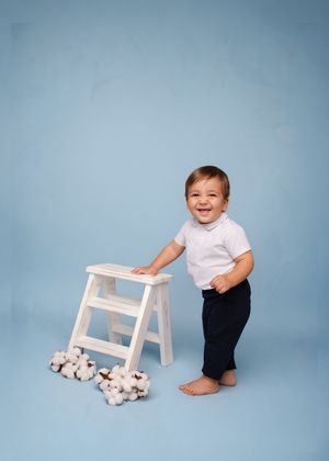 A series of three studio photos showing a toddler in white shirt and dark pants playing with a small white stool.