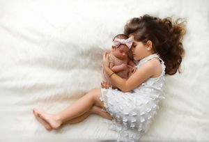 A baby wearing a white dress lies peacefully on soft white bedding while sleeping.