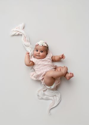 A baby in a pink floral dress and white diaper lies on a white background in four different poses.