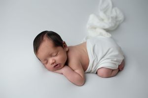 A sleeping newborn baby in white clothing lies peacefully on a soft gray background.