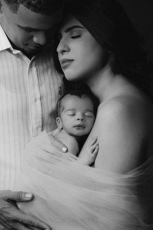 A tender black and white portrait of parents cradling their sleeping newborn baby wrapped in soft tulle fabric.