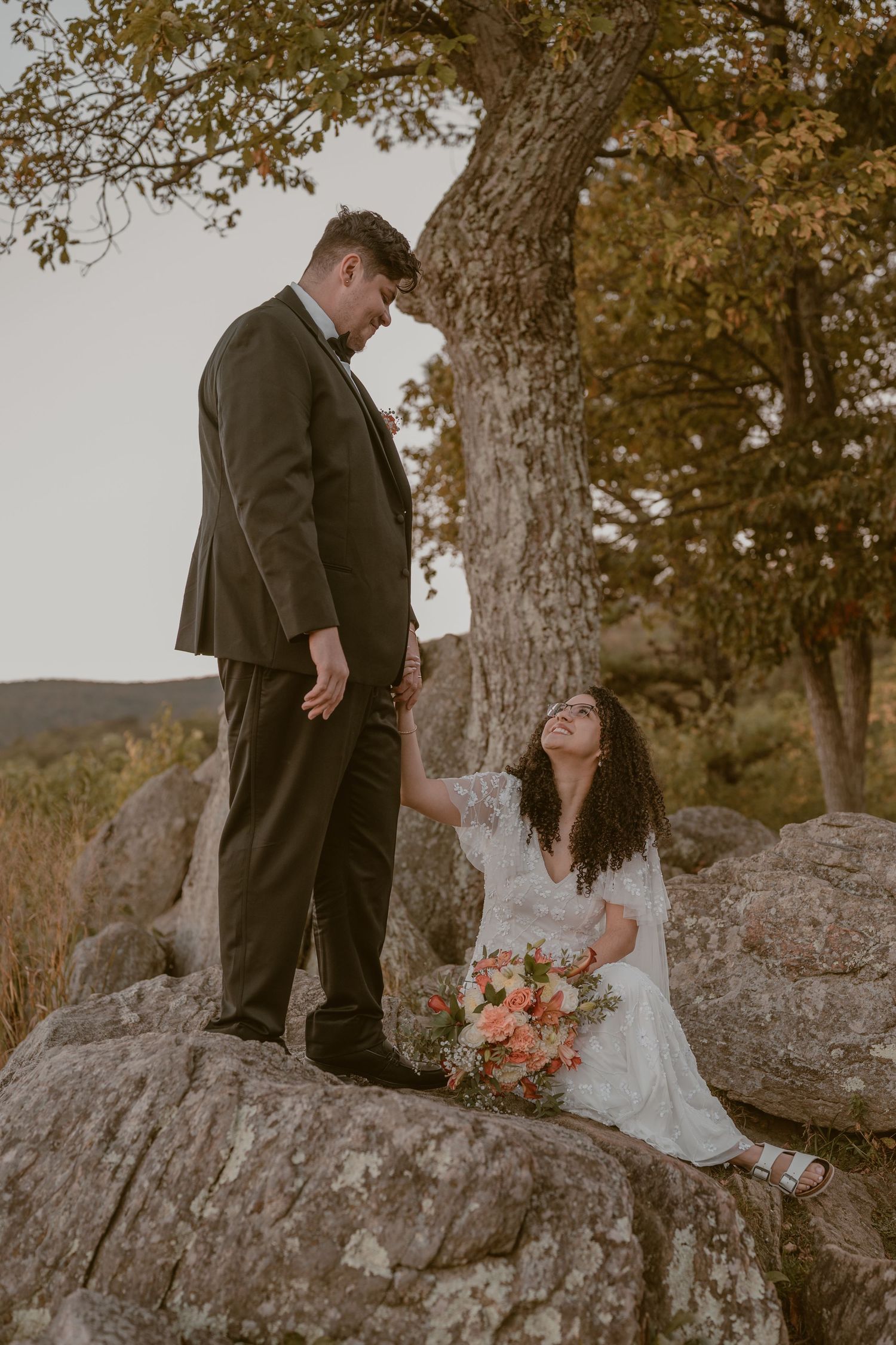 A couple shares a romantic moment on a rocky outcrop during their sunset wedding photoshoot in autumn.