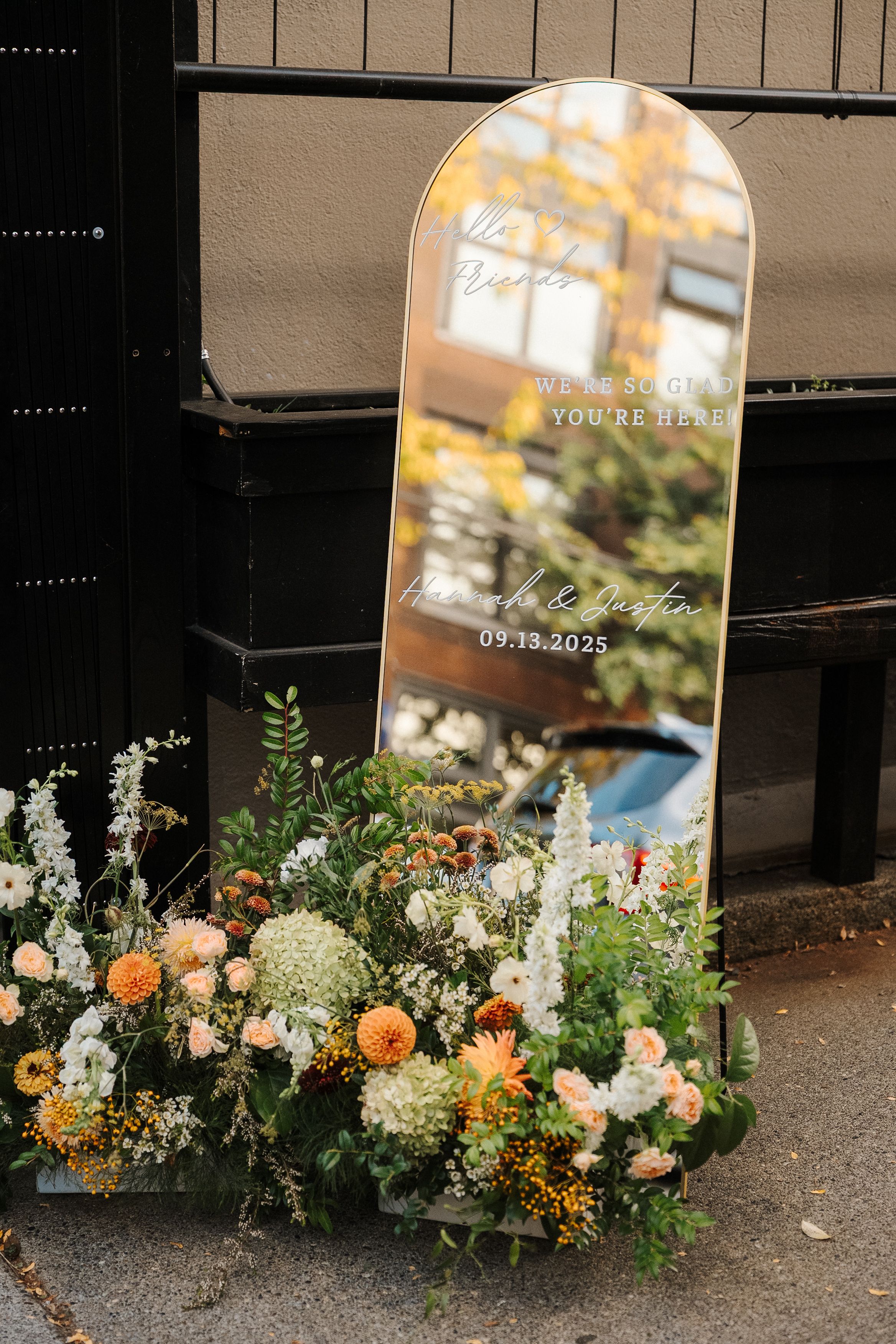 A decorative mirror with text writing surrounded by a beautiful arrangement of orange and peach flowers and greenery.
