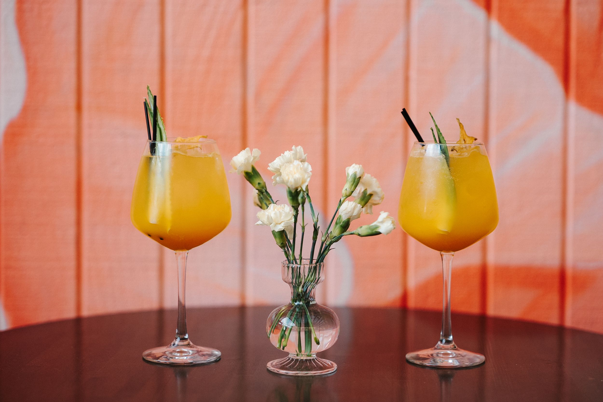 Orange-tinted event space with elegant cocktails and white floral arrangements on wooden tables.