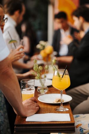 Orange cocktails and beer glasses on a wooden table at a social gathering.