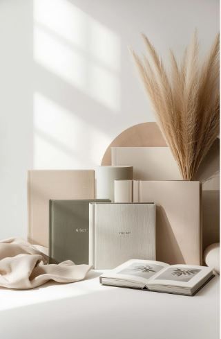 Minimalist beige aesthetic with perfume bottles, pampas grass, and an open book arranged on white surface with soft shadows.