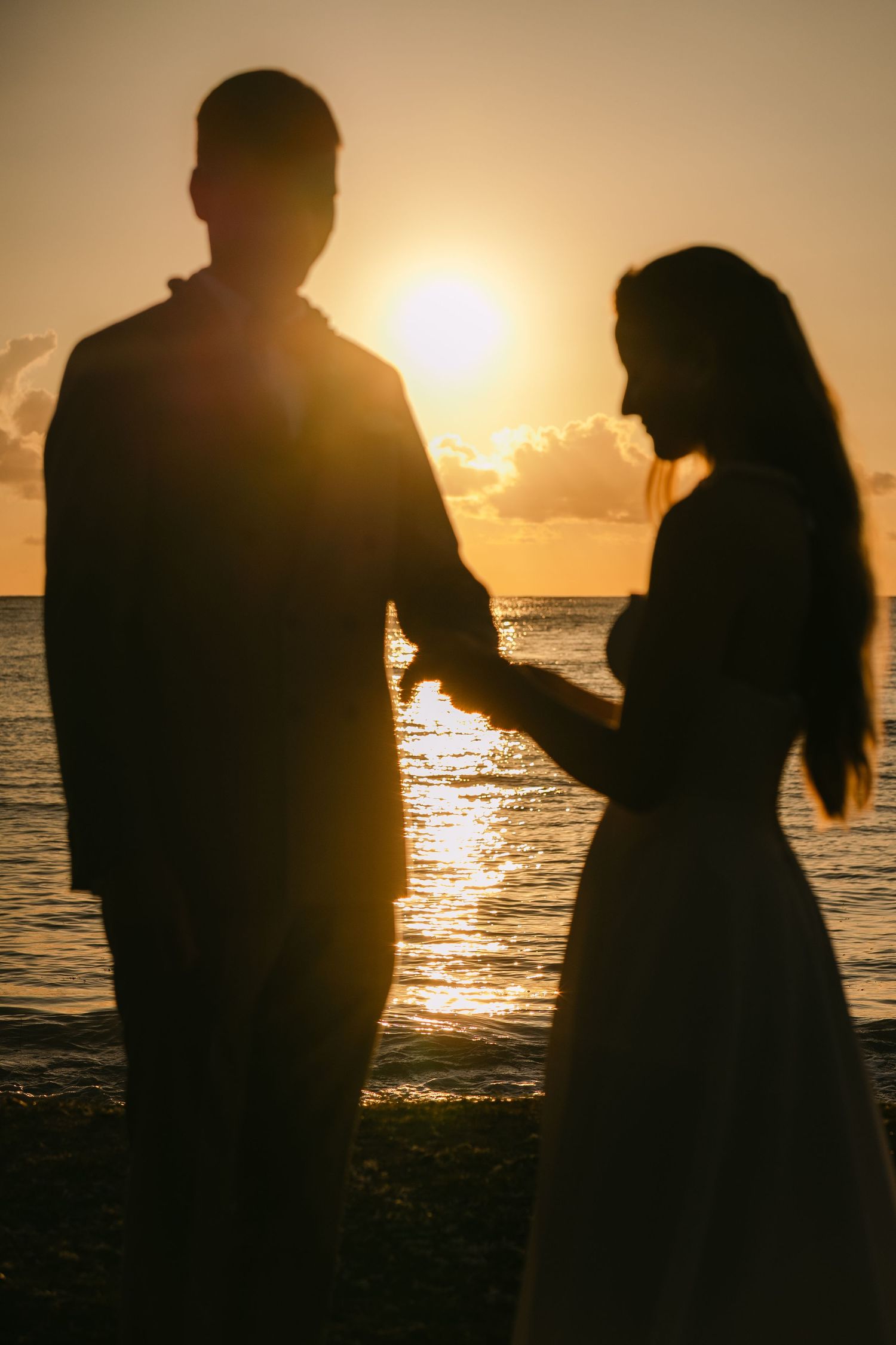 Silhouettes of surfers standing on beach at sunset with golden light reflecting off ocean waves.