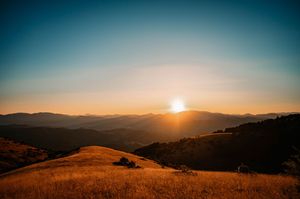 Monte Subasio landschap bij zonsopgang waar de zon net boven de bergen uikomt en de omgeving oranje kleurt.