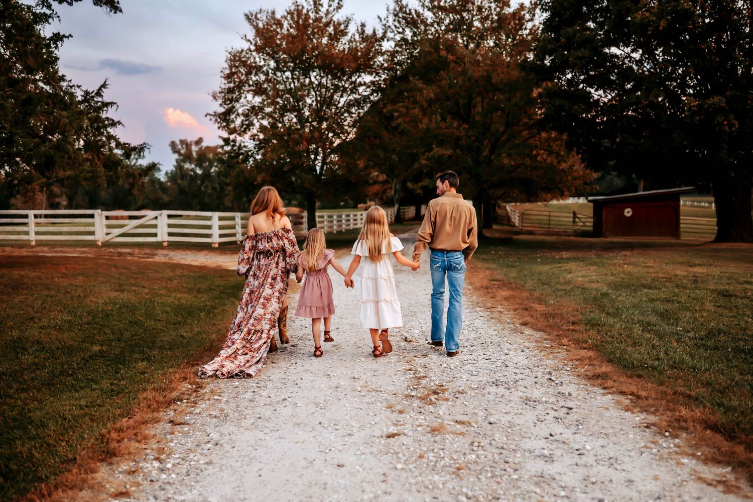 A group walking down a white gravel path surrounded by autumn trees and fencing at sunset.