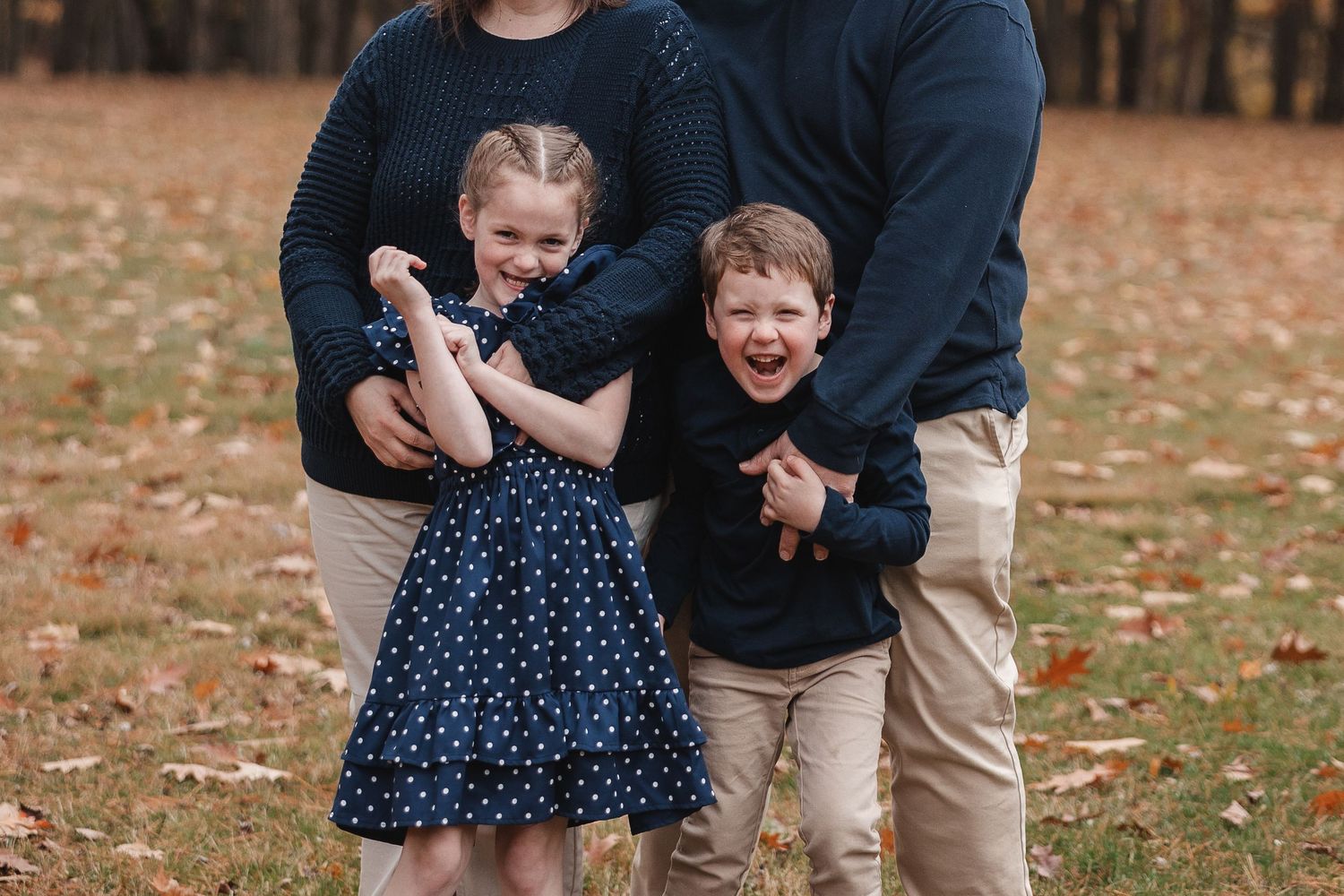 A family shares joyful moments together during an autumn photoshoot with fallen leaves in the background.
