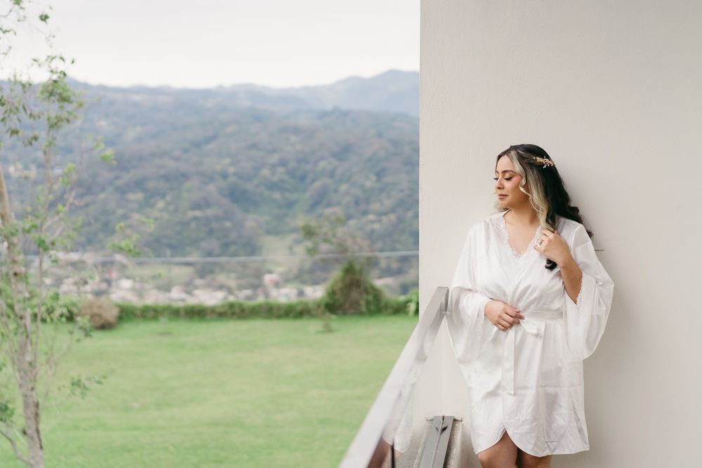 Bride in flowing white dress poses against scenic mountain backdrop in outdoor wedding photoshoot.