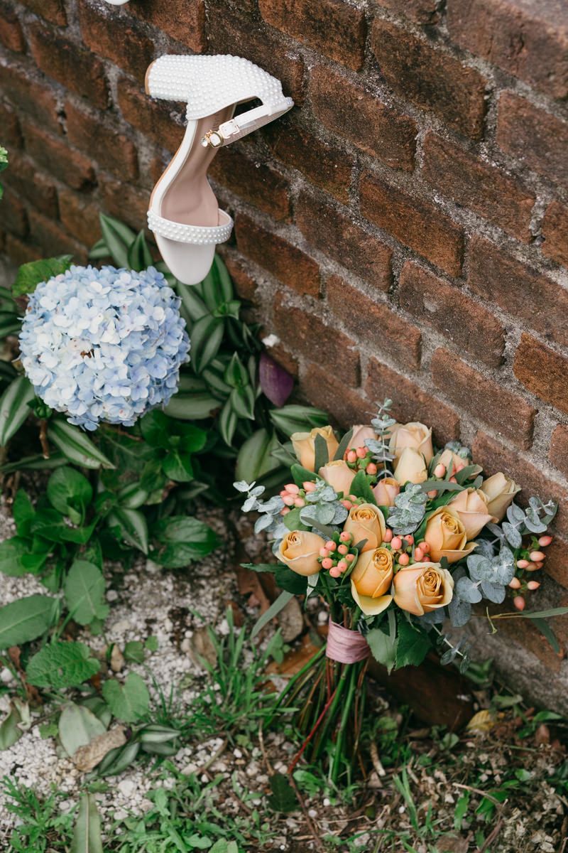 Delicate floral arrangement with peach roses and blue hydrangeas against a rustic brick wall.