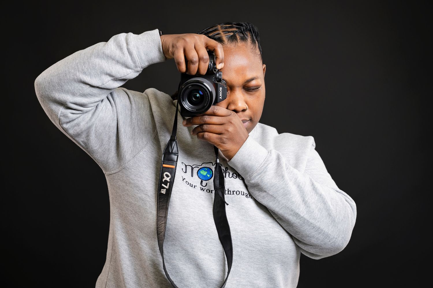 Professional photographer wearing a gray sweatshirt takes a photo with a DSLR camera against dark background.