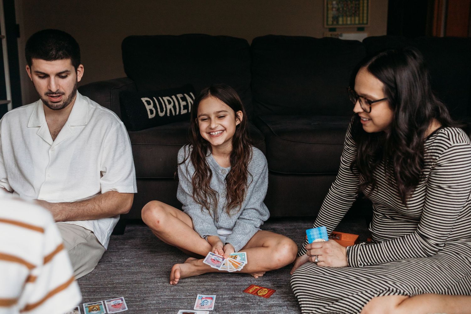 Friends sitting on the floor playing card games together in a casual home setting.