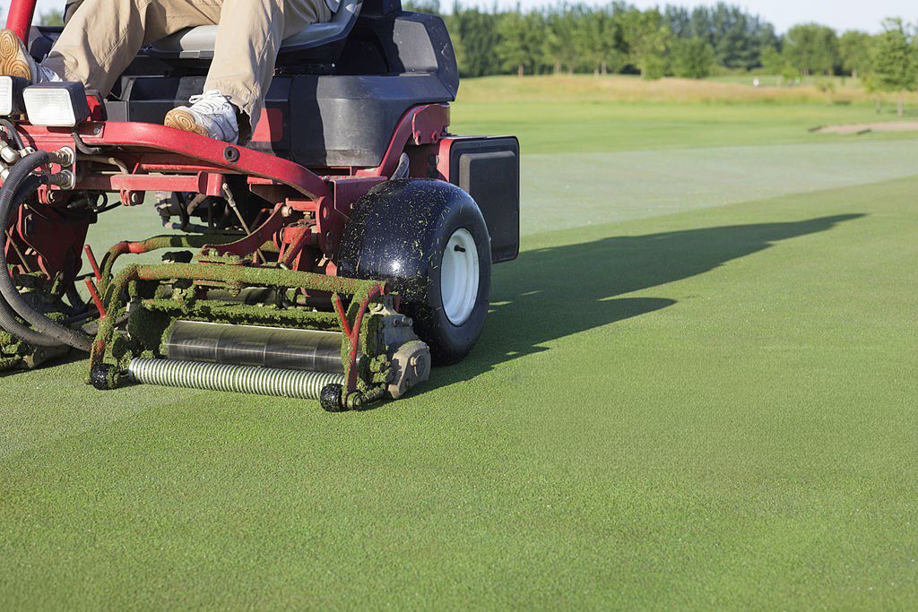 Red maintenance vehicle with specialized mowing equipment operates on a pristine golf course putting green.