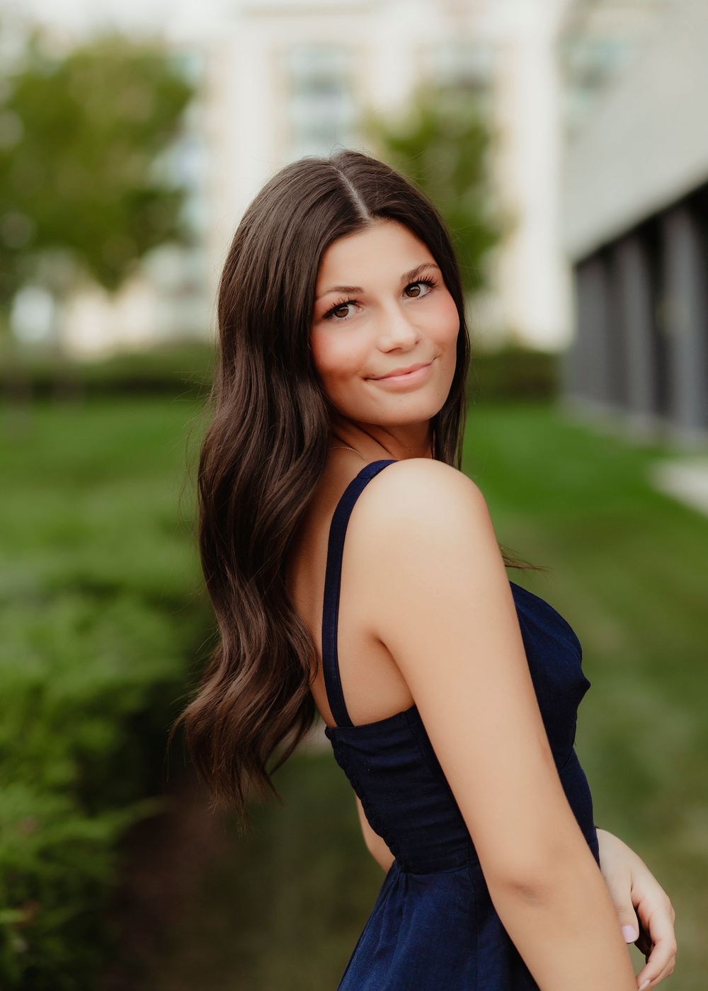 Woman in navy dress poses against architectural background with landscaping.