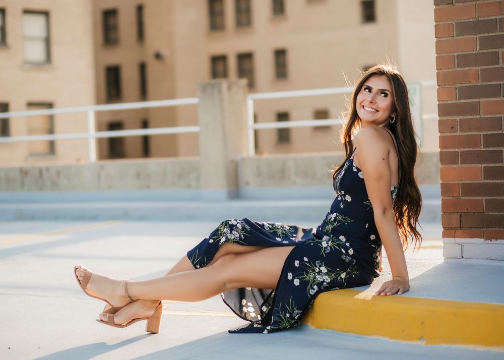 Woman in floral dress poses elegantly against urban backdrop on rooftop.