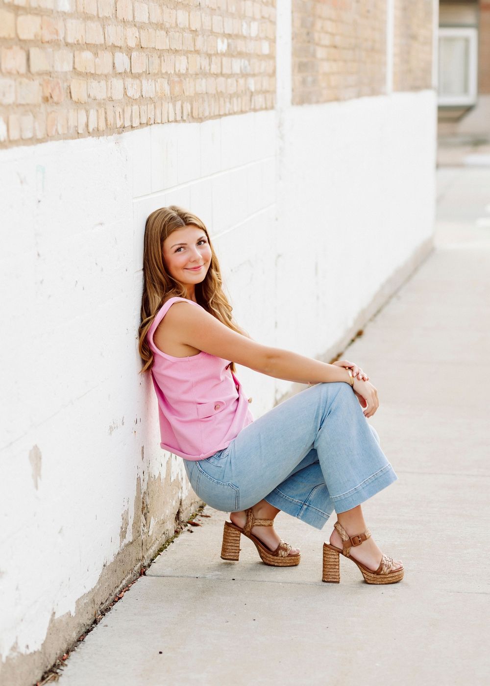 Casual street style portrait against white brick wall wearing pink top and jeans.