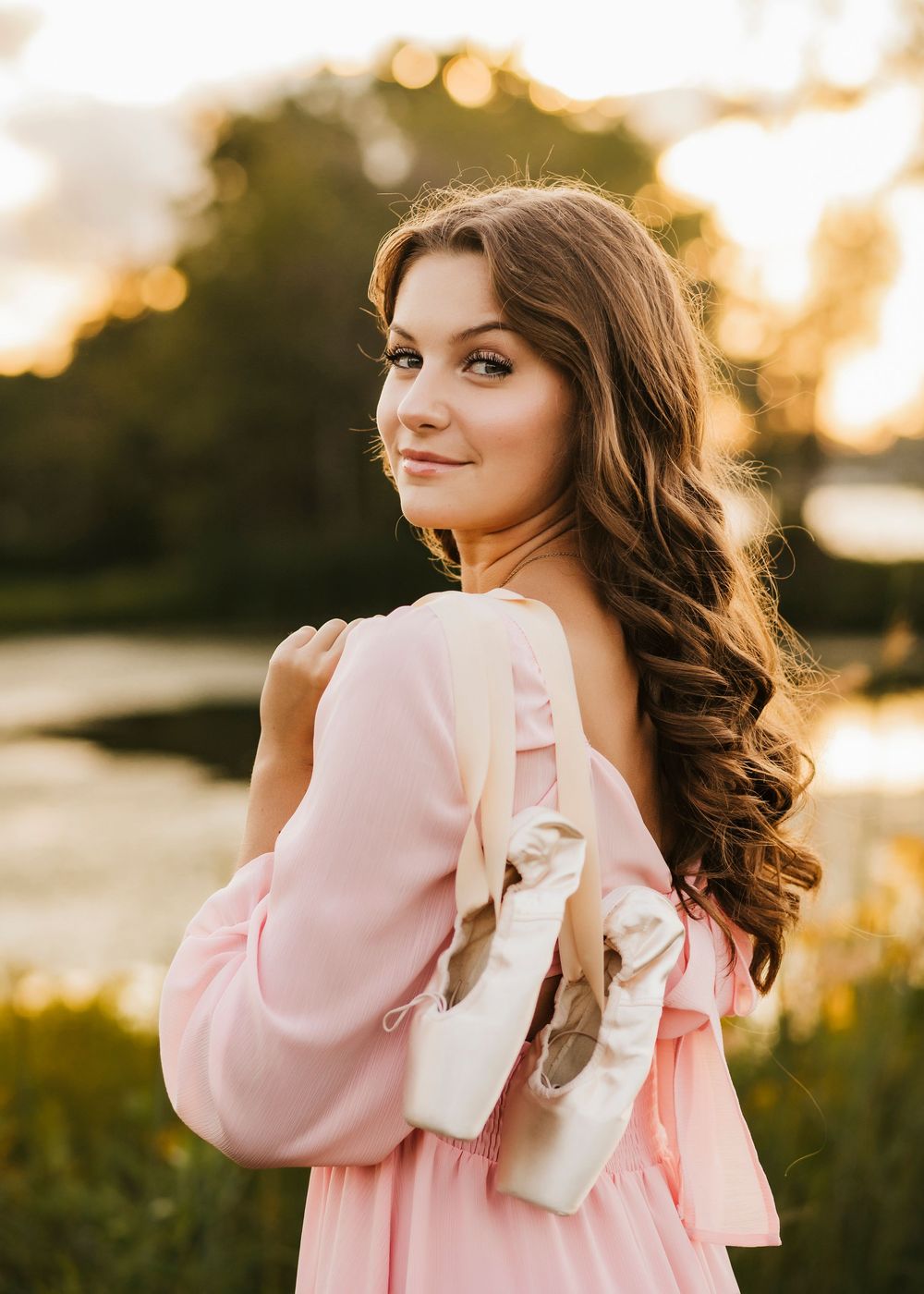 Artistic portrait featuring ballet shoes and a flowing pink dress in warm evening light.