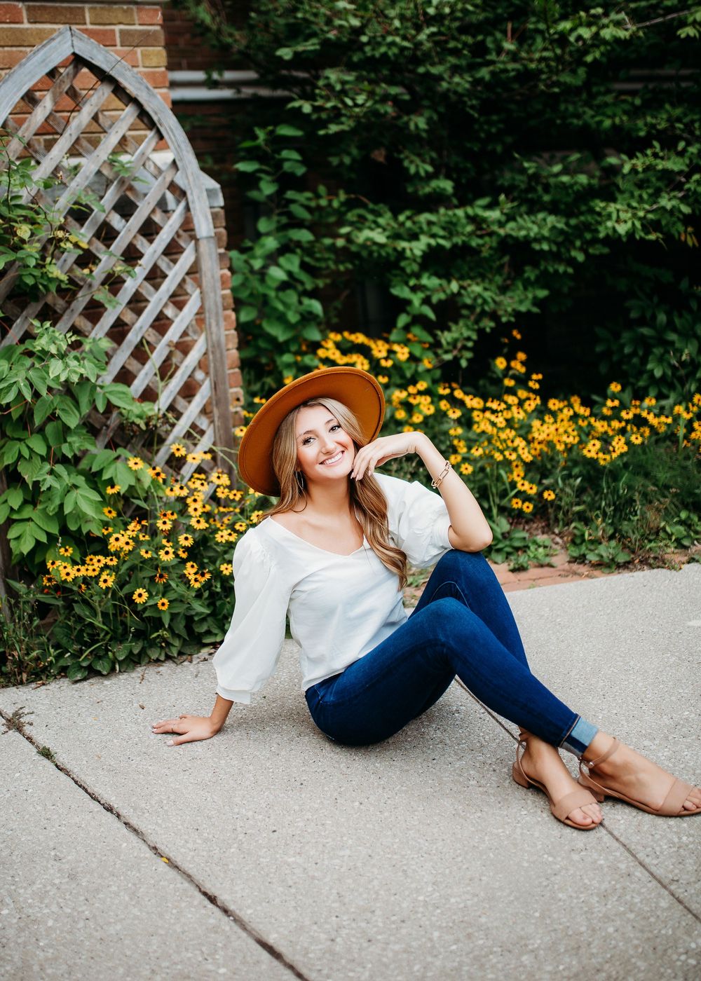 Relaxed outdoor photography featuring white top and jeans near garden trellis with yellow flowers.
