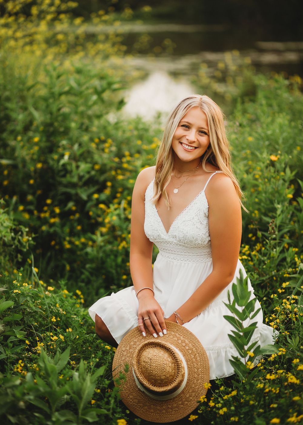 Woman in white dress holding straw hat while standing among yellow wildflowers.