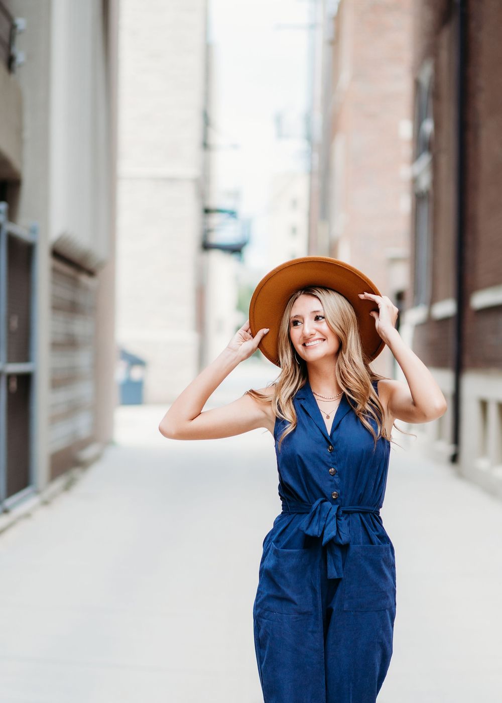 Playful fashion poses in navy blue dress and brown hat against urban backdrop.