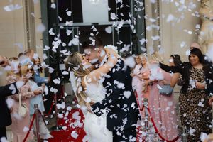 Wedding celebration with white confetti flying through the air as guests celebrate outside a venue.