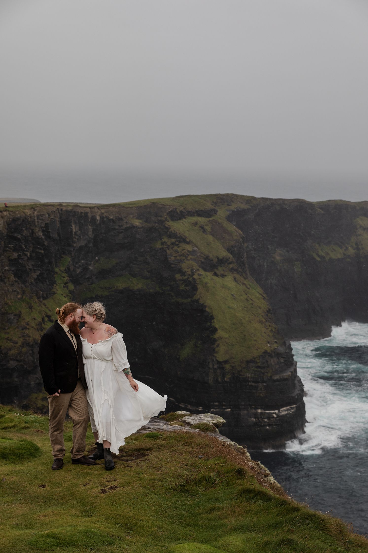 Bride and groom holding hands during dramatic Irish weather at Hags Head coastline