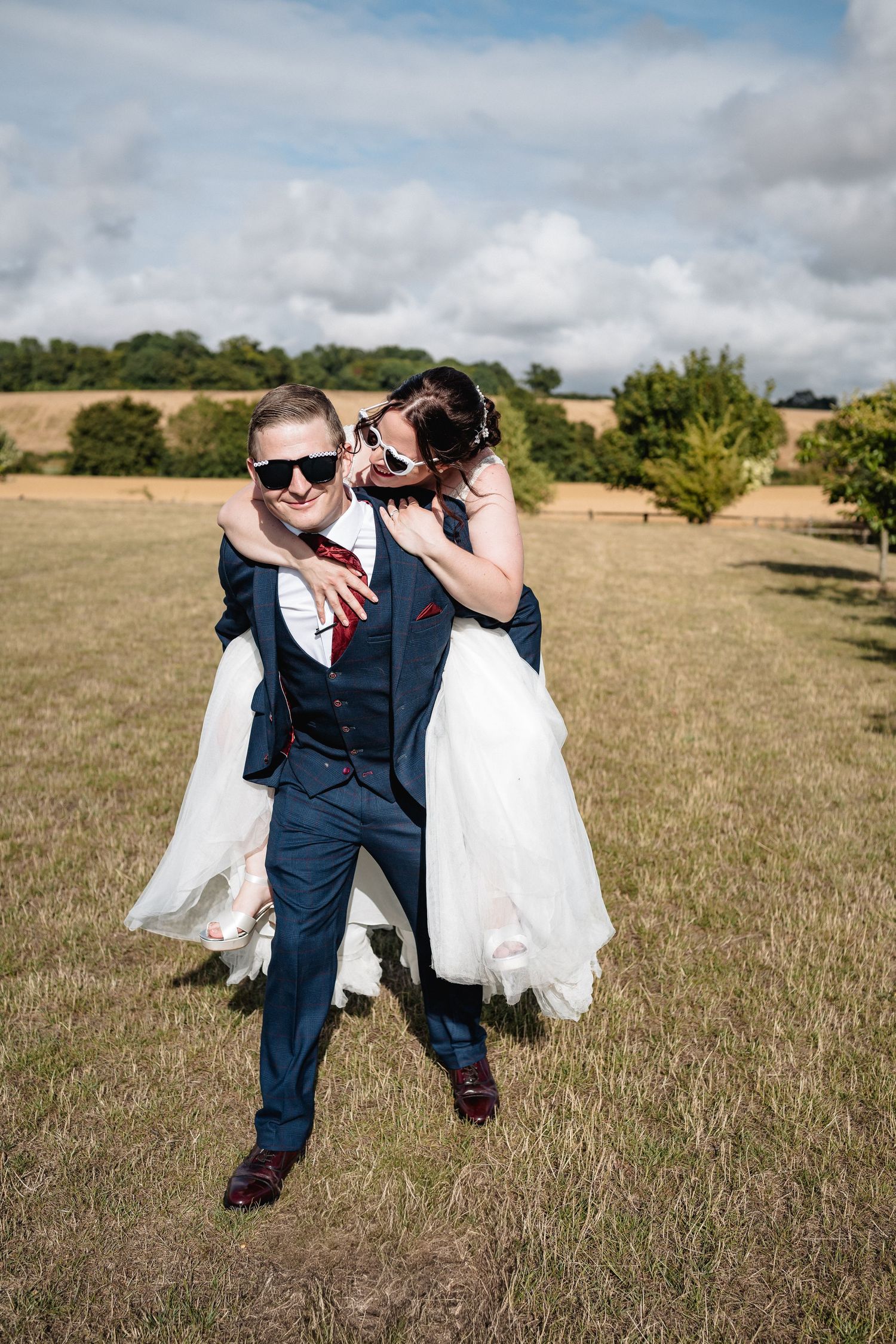 A couple in wedding attire shares a romantic moment in a rustic field under cloudy skies.
