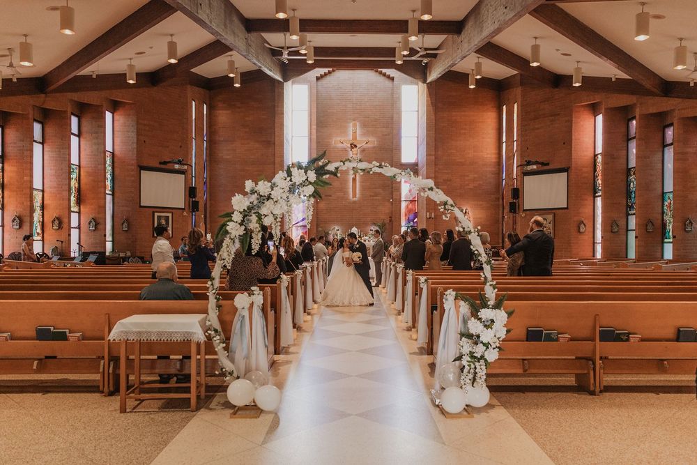 Beautiful church wedding aisle decorated with white floral arch and balloon arrangements for ceremony.