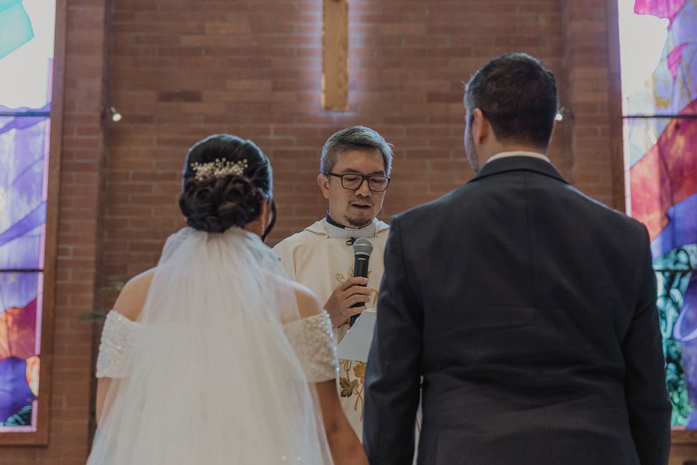 Catholic priest reading vows to bride in white dress and groom during church wedding ceremony.