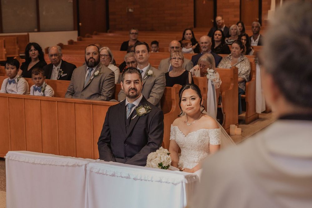 Bride and groom sitting attentively before priest during traditional Catholic church wedding ceremony.