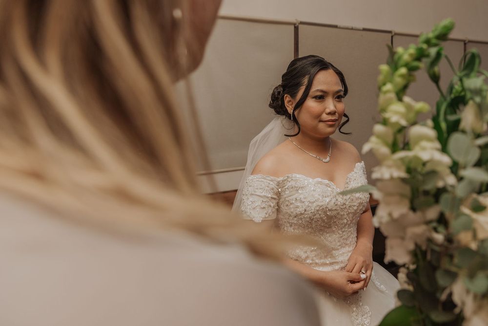Beautiful bride in off-shoulder lace wedding gown smiling during pre-ceremony preparations.