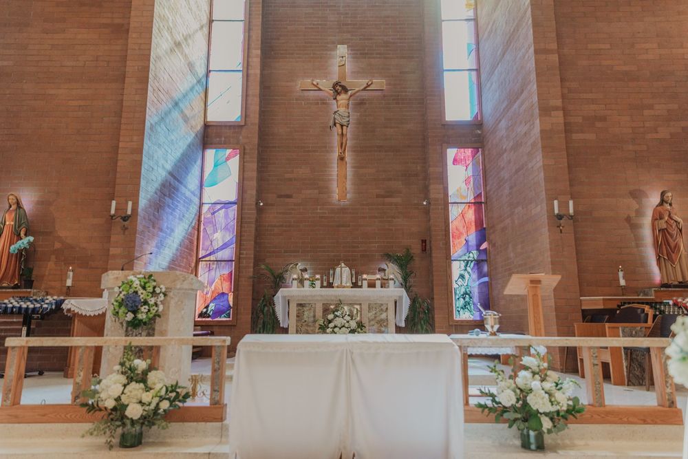 Stunning Catholic church altar decorated with white flowers beneath crucifix and colorful stained glass.