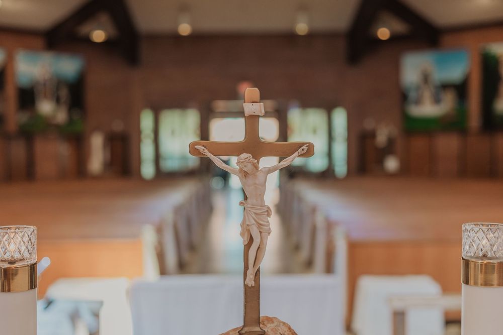 A golden crucifix stands on an altar in a softly lit Catholic church with pews and stained glass windows.