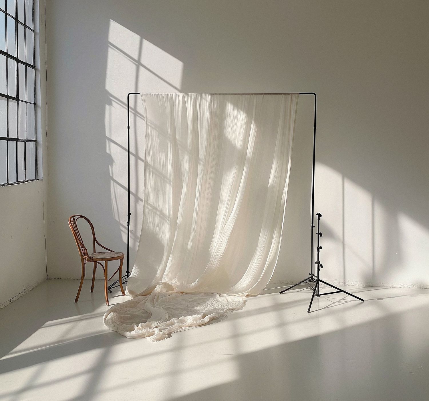 Minimalist photography studio setup with natural light streaming through windows and a wooden chair against a white wall.