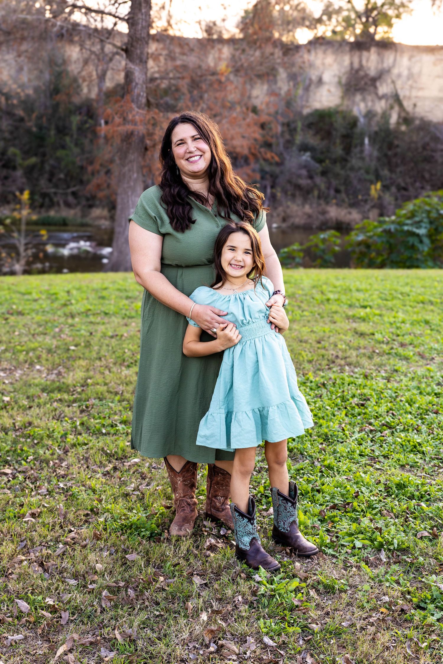 Mother and daughter in dresses and boots posing together outdoors near a rocky cliff.