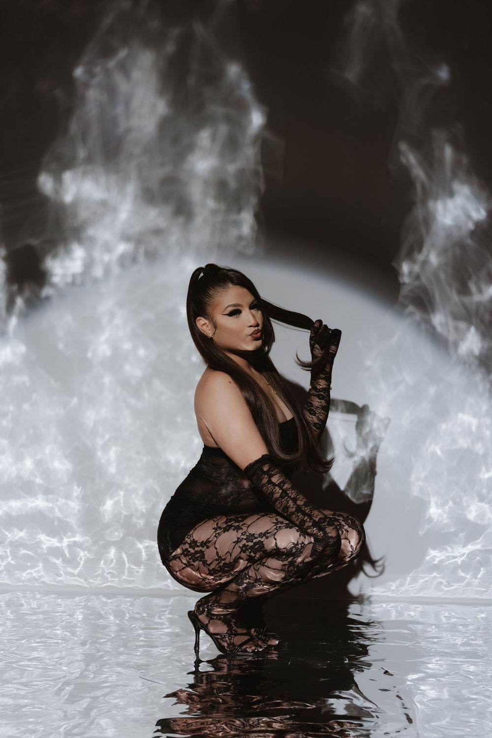 A figure in black lace poses dramatically in shallow water with ethereal smoke effects in the background.
