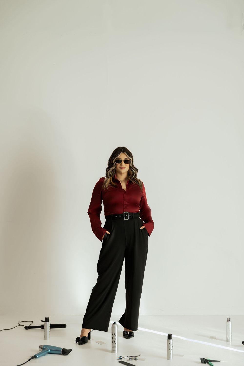 A fashion model poses in a burgundy top and black wide-leg pants against a white studio backdrop.