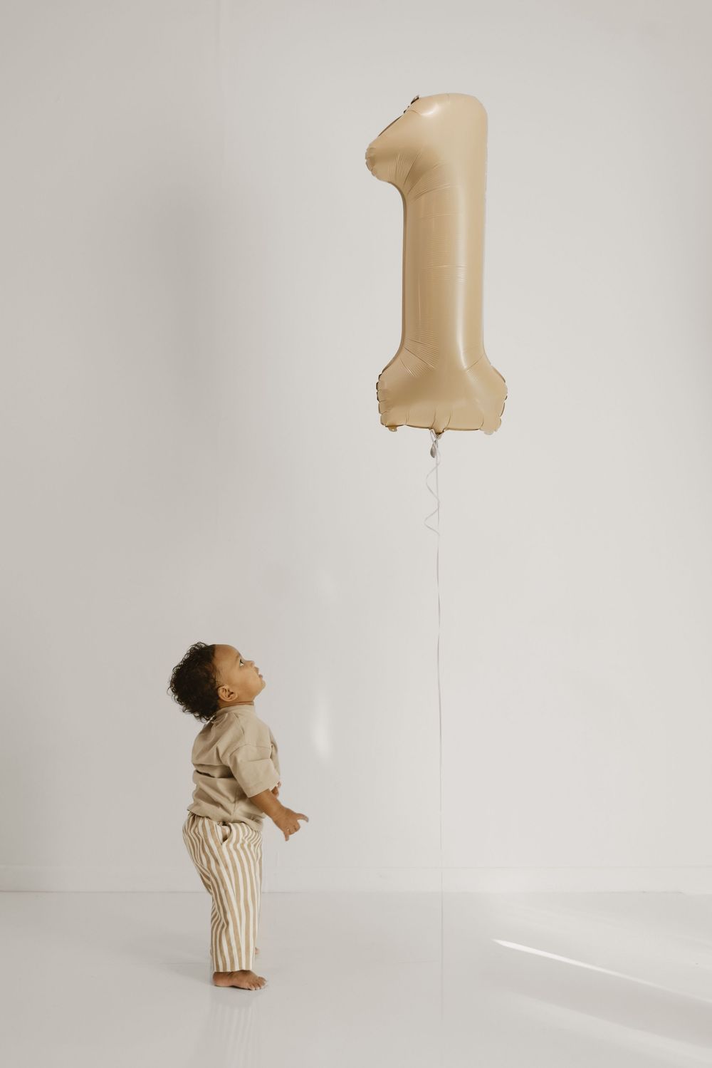 A series of minimalist photographs showing a small child in striped clothing playing against a white wall with soft lighting.