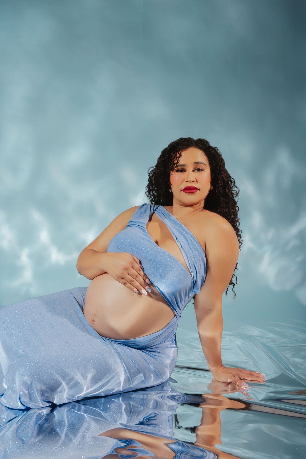 A maternity photoshoot features a person in a flowing light blue dress posing gracefully against a dreamy background.