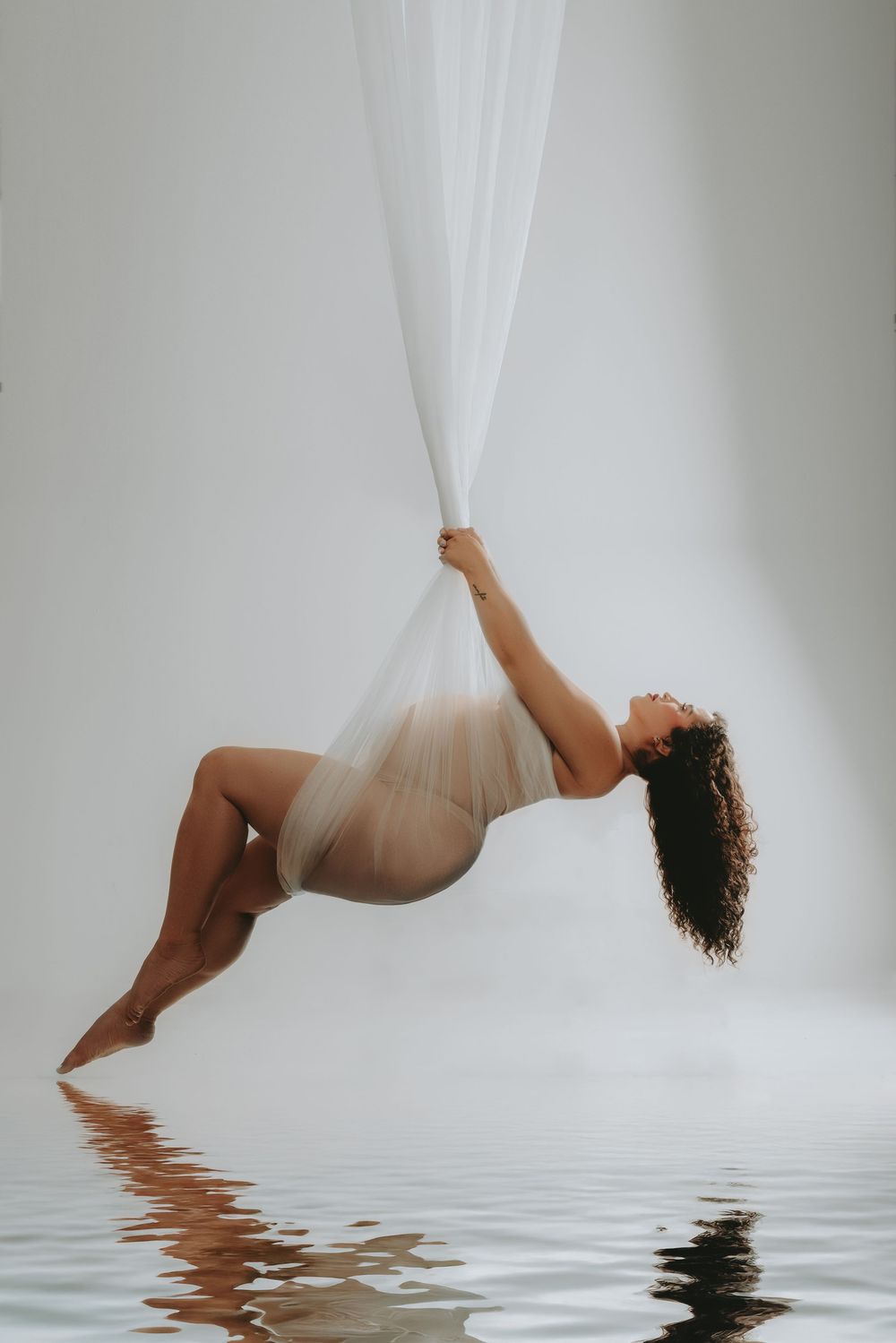 Artistic portrait of a figure draped in white fabric floating above reflective water in ethereal lighting.