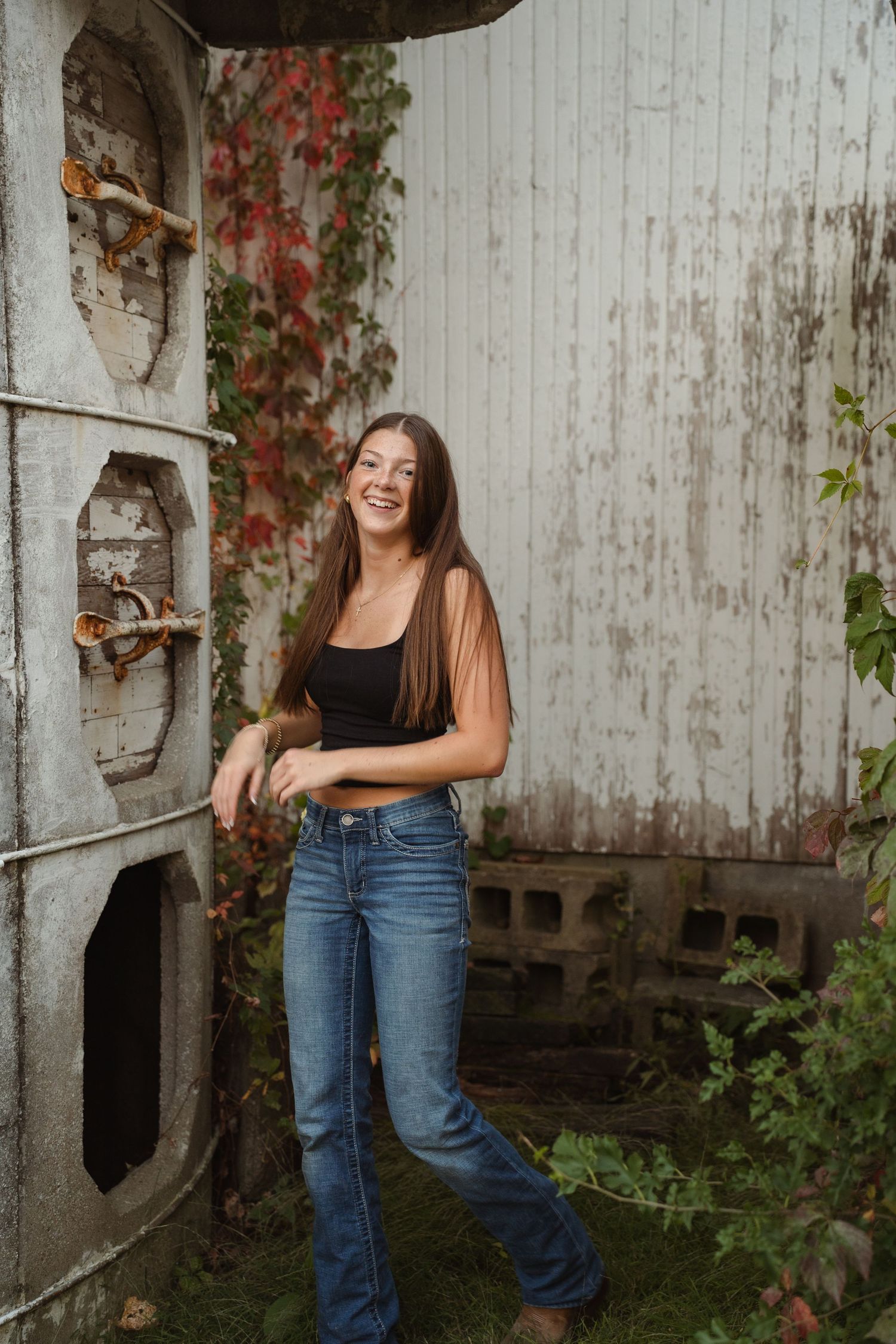 Person standing by weathered silo wall with climbing vines in casual attire.
