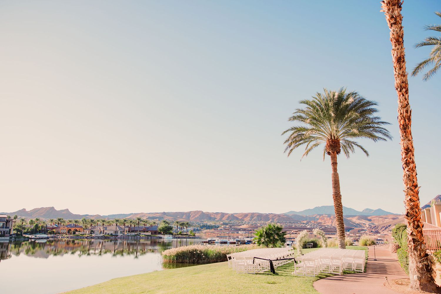 Palm trees line a waterfront path with desert mountains and homes in the background at Lake Havasu, Arizona.