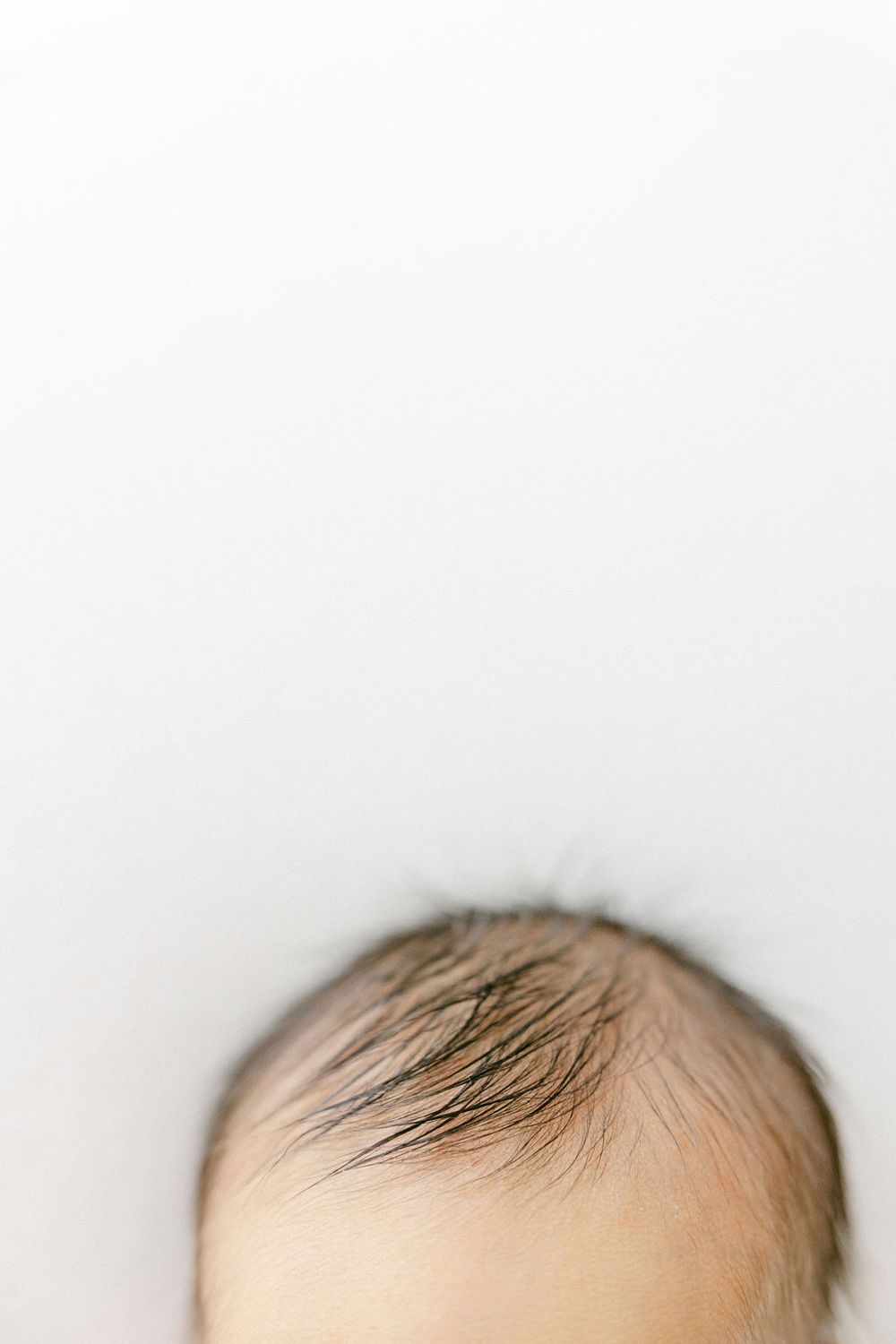 Top view of soft wispy baby hair against white background showing natural growth pattern. Connecticut Newborn Photography.