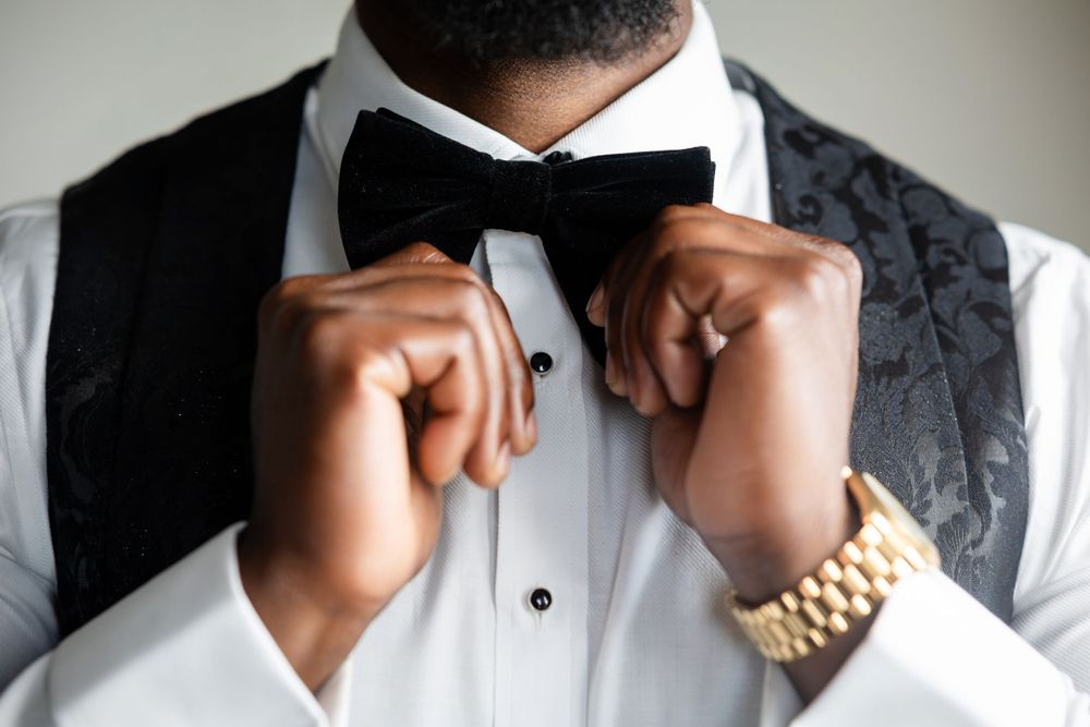Close-up of hands adjusting a black bow tie with gold watch visible.