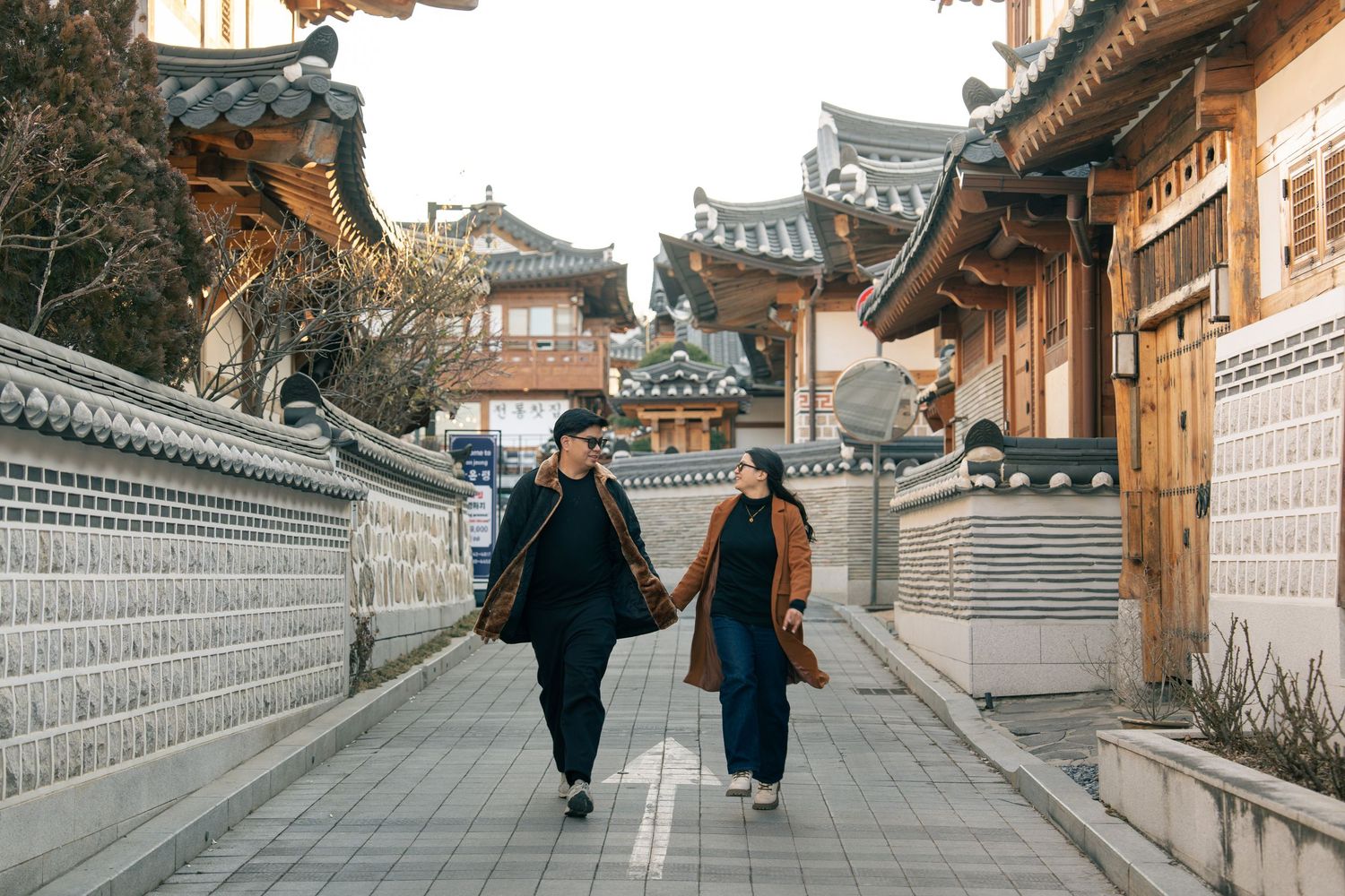 Two people walking down a traditional stone-paved alley in Bukchon Hanok Village, Seoul, surrounded by historic architecture.