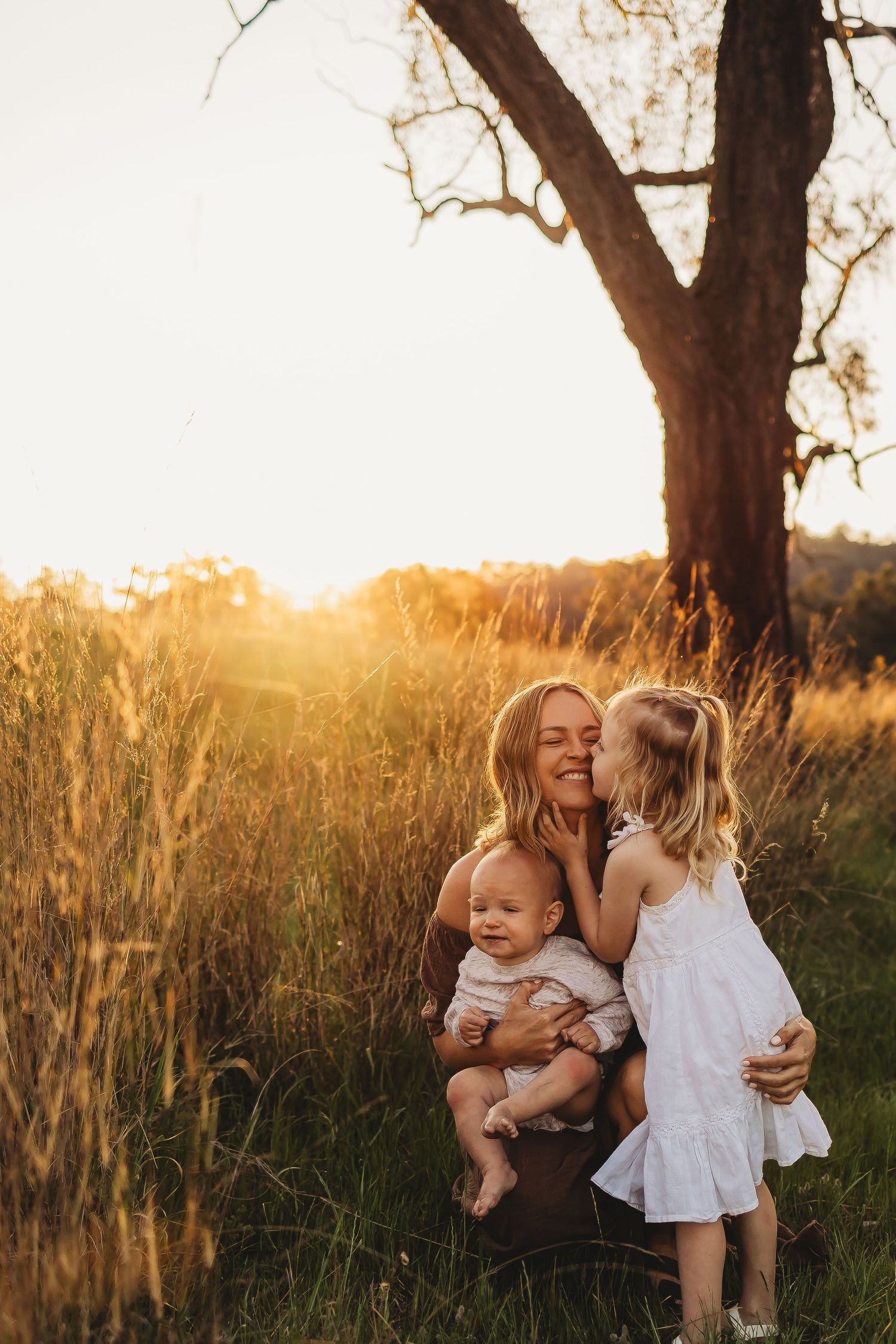 Family shares tender moments together in golden sunlit field during sunset photo session.