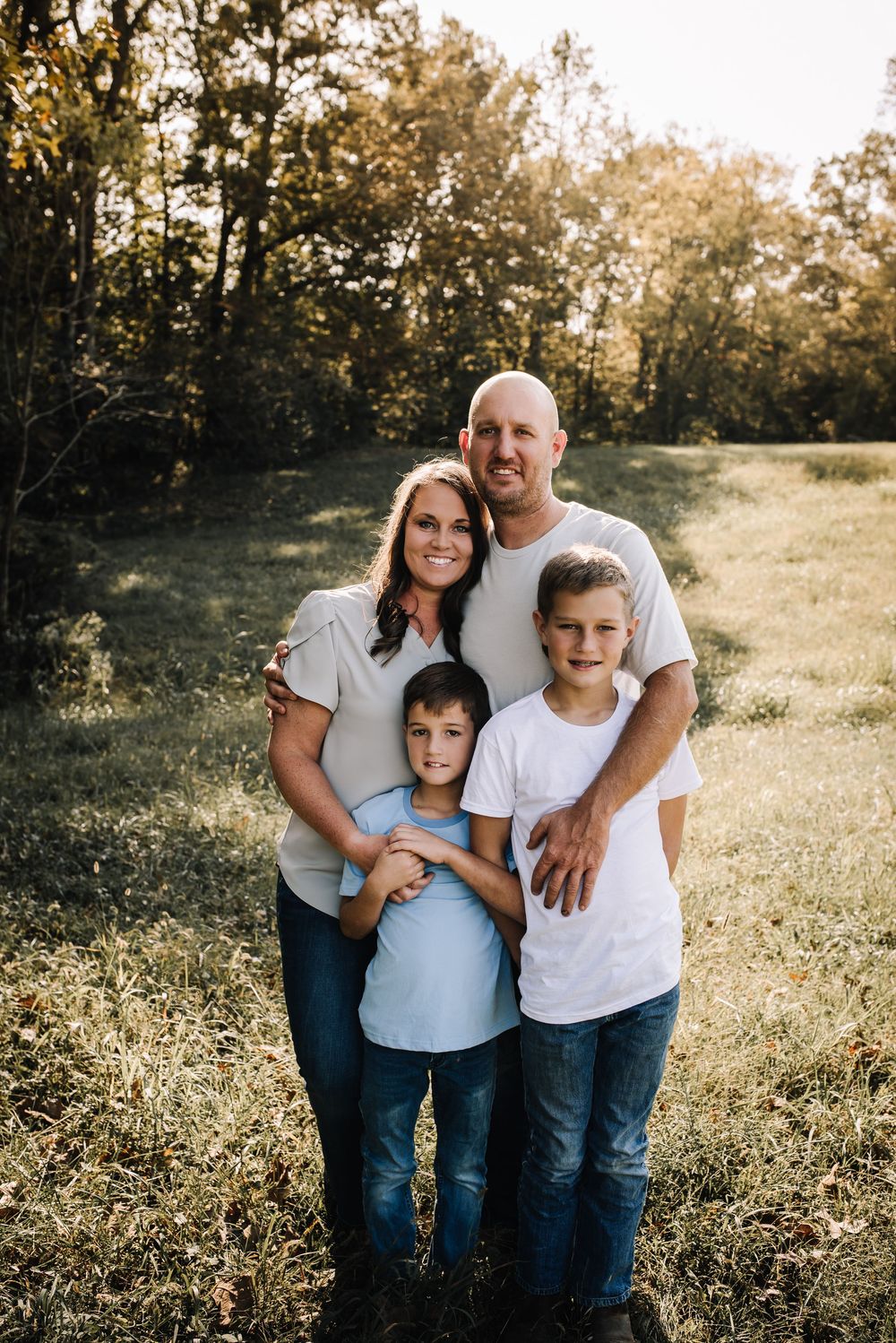 Family enjoying a warm sunset together in a grassy field wearing casual white shirts and jeans.